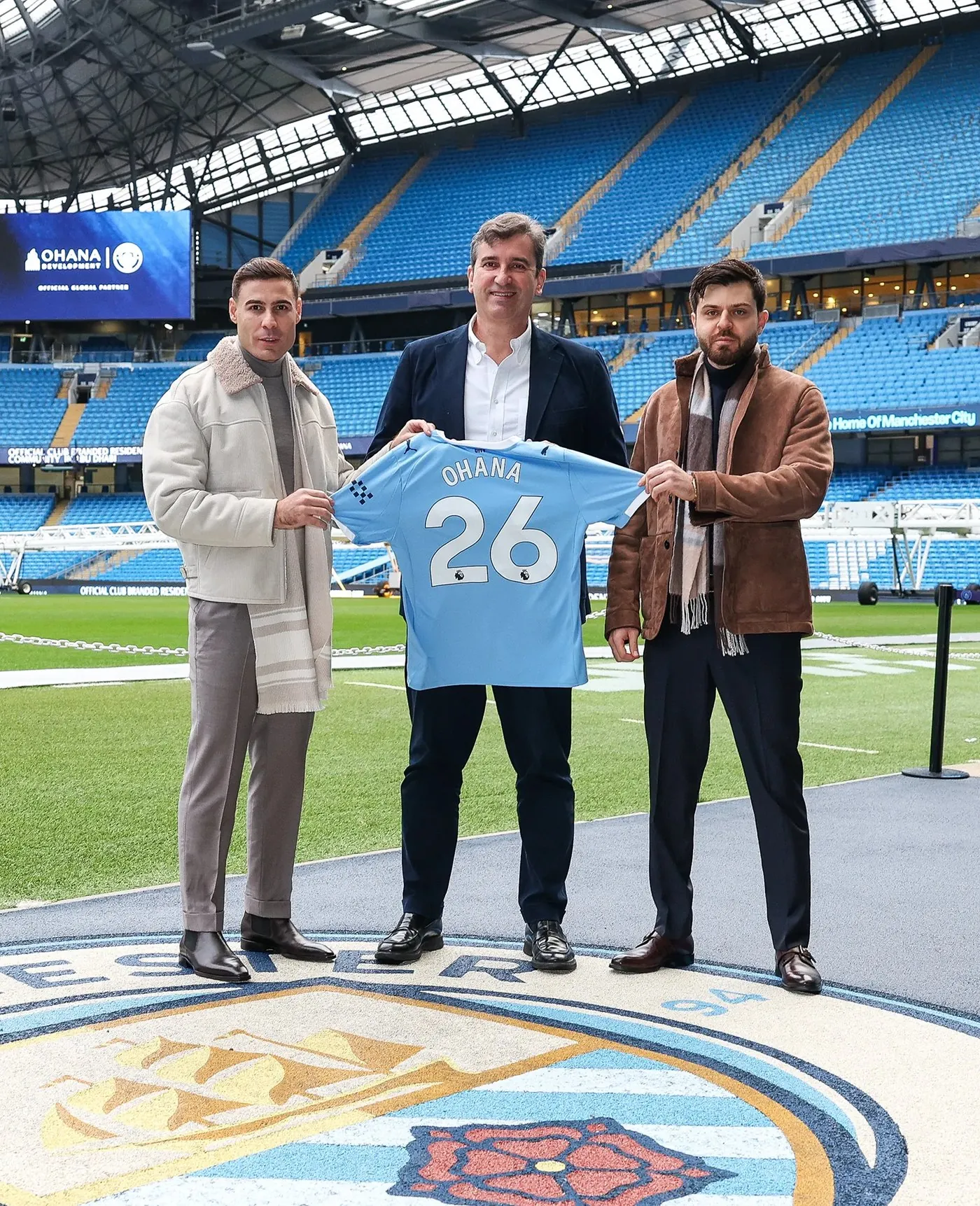 Ohana Development and Manchester City executives with a club shirt on the pitch at the Etihad Stadium